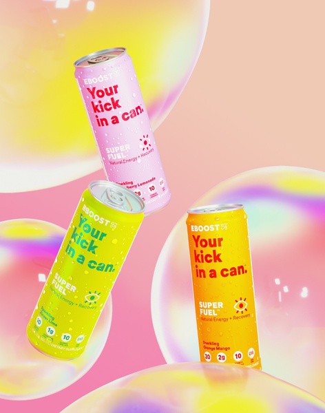 A high-energy product display featuring three colorful energy drink cans floating among iridescent bubbles against a soft pink background.